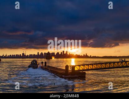 Speedboat leaves from the dock as the golden sun sets behind the downtown Vancouver skyline and horizon with sunbeam reflecting on the water of Bur... Stock Photo