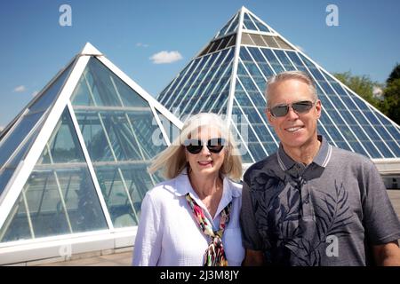 Outdoor portrait of a mature couple wearing sunglasses with modern architecture in the urban background; Edmonton, Alberta, Canada Stock Photo
