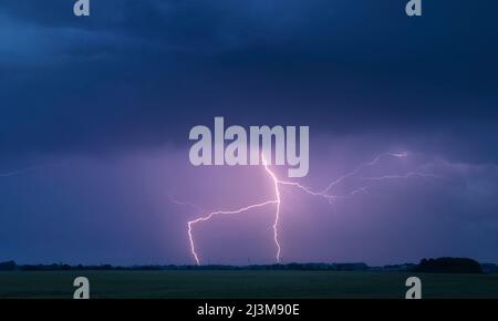 A lightning bolt arcs out of the base of a dark storm cloud and strikes ...