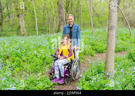 Girl in a wheelchair with her friend posing in the forest area while looking at wildflowers by the Potomac River Stock Photo