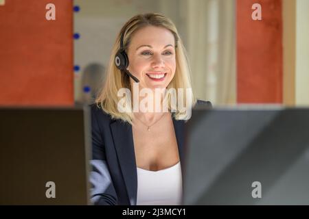 Successful female entrepreneur working on desktop computer while using a headset for conversation in modern office Stock Photo