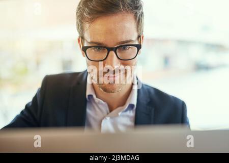 He seems quite pleased with himself. Shot of a young businessman using his laptop while sitting in a coffee shop. Stock Photo