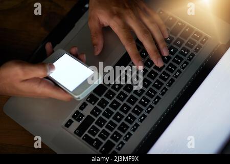 Hell crack that code. High angle shot of a hacker using a cellphone to cracking a computer code in the dark. Stock Photo