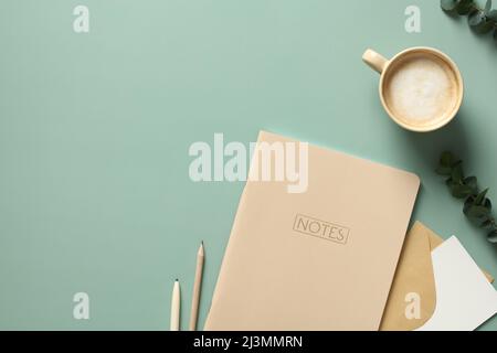 Minimal elegant office desk table with weekly planner, cup of coffee, eucalyptus leaves on green background. Flat lay, top view, copy space. Stock Photo