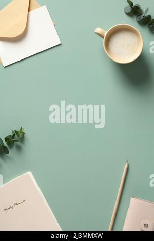 Vertical banner of home office desk table with cup of coffee, paper notebook, eucalyptus leaves. Flat lay, top view. Stock Photo