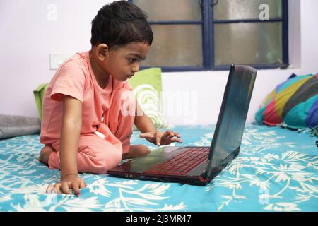 a toddler baby boy engaged in watching and exploring laptop.Screen time addiction concept image. Stock Photo