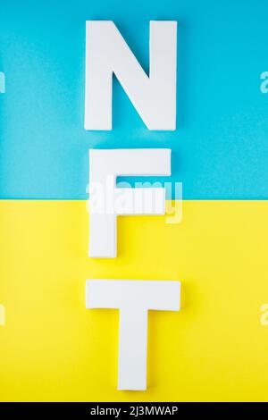 NFT inscription with white 3d letters on a blue-yellow background. Non-fungible token against background of colors of the Ukrainian flag. Crypto art c Stock Photo