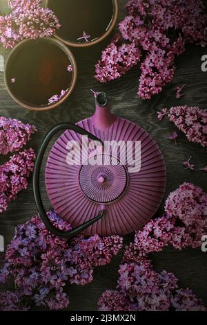 Teapot and two cups of tea on the dark wooden table decorated with blooming lilac, top view Stock Photo