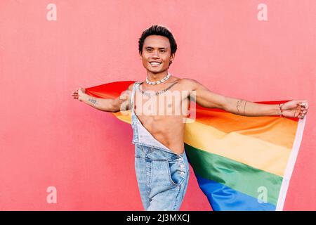 Young happy man walking outdoors with a rainbow LGBT flag looking away Stock Photo