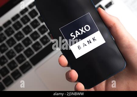 Poltava, Ukraine - April 9, 2022: Saxo Bank app. Trader and broker application. Mobile phone in hand close-up view Stock Photo