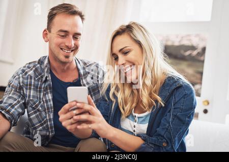 Look at this funny text I just got. Shot of a young couple using a cellphone at home. Stock Photo