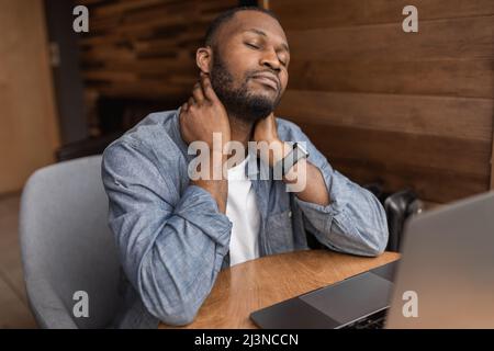 Tired businessman is sitting at the desk, having a back ache. Exhausted male freelancer is using computer, having a tense brainstorm while developing Stock Photo