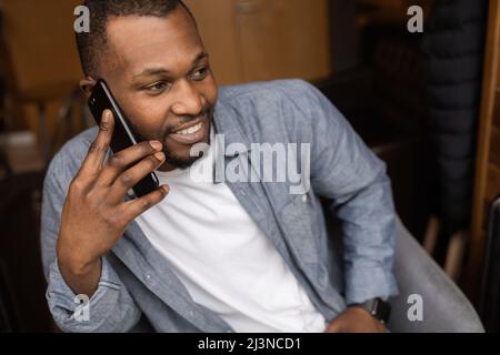 Close-up portrait of happy African American young man having fun talking on cell phone in office, looking to the side. Delighted with good news, he ha Stock Photo