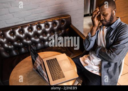 Frustrated stressed african american businessman using laptop, frustrated unhappy young man touching head sitting with closed eyes hearing bad news by Stock Photo