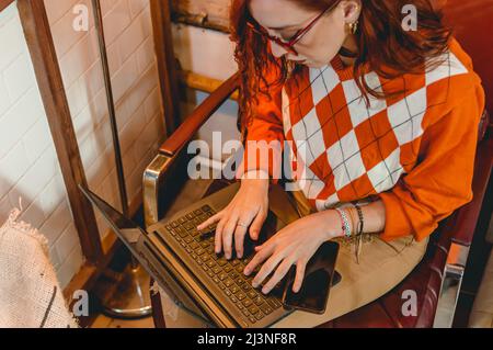 top view of caucasian young business woman working typing on laptop keyboard, sitting in restaurant, negotiating and sharing internet. Stock Photo