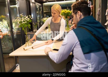 female florist wrapping flowers in paper in a flower shop for a customer Stock Photo