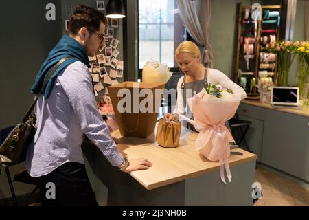 a customer in a flower shop picks up a fresh bouquet prepared by a florist and wrapped in gift paper Stock Photo