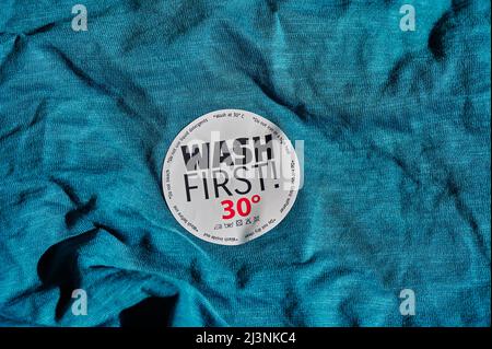 Sticker on a T-shirt with washing instructions and the text 'Wash first'. Stock Photo
