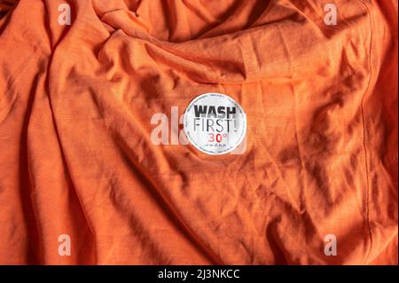 Sticker on a T-shirt with washing instructions and the text 'Wash first'. Stock Photo