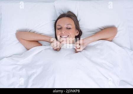 Good morning. Top view of beautiful young woman wakening up happy in the white bed. Day off work Stock Photo