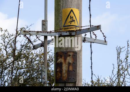 A Danger of Death warning sign mounted on a wooden pole above a metal and barbed wire unit to deter climbing Stock Photo