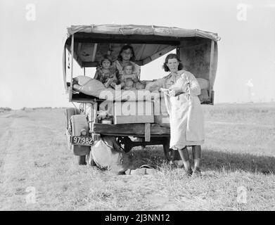 Family between Dallas and Austin, Texas. The people have left their home and connections in South Texas, and hope to reach the Arkansas Delta for work in the cotton fields. Penniless people. No food and three gallons of gas in the tank. The father is trying to repair a tire. Three children. Father says, &quot;It's tough but life's tough anyway you take it&quot;. Stock Photo