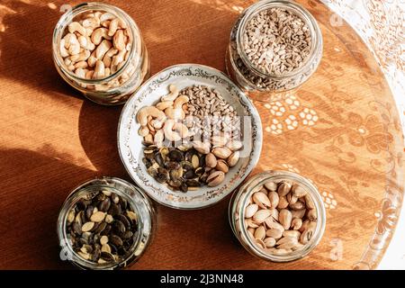 Cashew nuts, pistachios, sunflower seeds and pumpkin seeds in a glass jars and porcelain bowls on the table. Healthy snacks Stock Photo