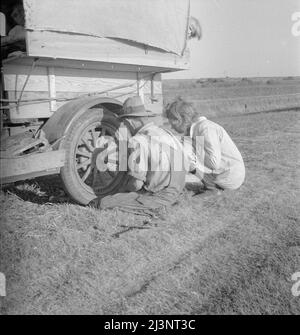 Family between Dallas and Austin, Texas. The people have left their home and connections in South Texas, and hope to reach the Arkansas Delta for work in the cotton fields. Penniless people. No food and three gallons of gas in the tank. Father is trying to repair a tire. Three children. Father says, &quot;It's tough, but life's tough anyway you take it&quot;. Stock Photo