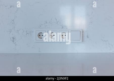 Block of three sockets and a switch on a white wall Stock Photo