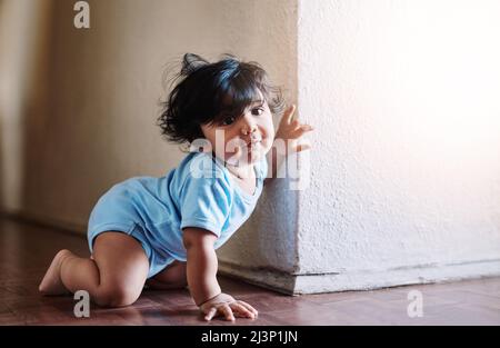 Looks whos around the corner. Shot of a little baby boy playing and hiding around a corner at home during the day. Stock Photo