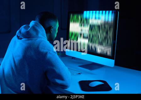 Hes always sticking to the code. Shot of a young male hacker cracking a computer code in the dark. Stock Photo