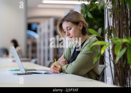 Academic career. Female university professor taking notes in day planner while sitting in library Stock Photo