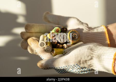 Close up of female hands in cotton protection gloves holding used alkaline batteries heap Stock Photo