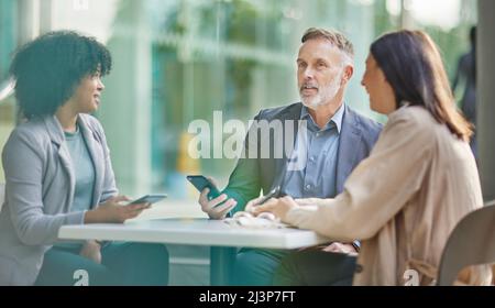 You make a dynamite team. Shot of a group of colleagues brainstorming ideas at a coffee shop while using their smartphones. Stock Photo