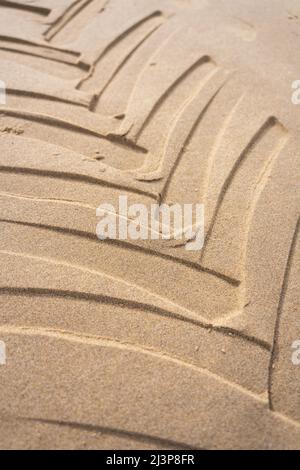 Tractor tyre prints embedded into sandy beach with geometric pattern. Vehicle tyre tracks close up with sandy texture at seaside. Stock Photo