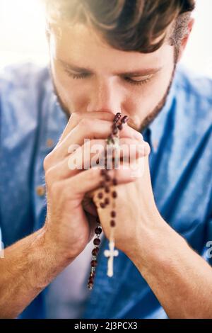 Putting his faith first. Cropped shot of a young man holding his rosary while praying. Stock Photo