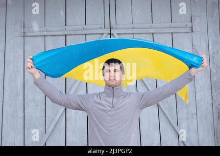 A man holds the state flag of Ukraine outdoors in snowy weather. Ukrainian flag, patriotism. Defender of the country, his land and family. Ukrainians against the war. Stock Photo