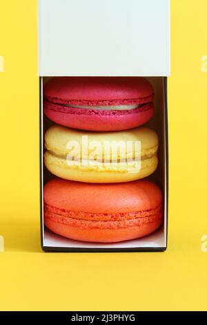 Multicolored macarons in a cardboard box with an open lid standing upright on a yellow background. Closeup Stock Photo