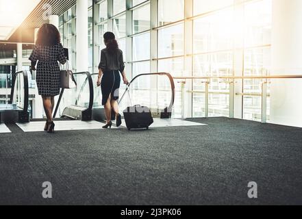 You gotta go where business calls. Rearview shot of two unrecognizable businesswomen going on an escalator in a modern workplace. Stock Photo