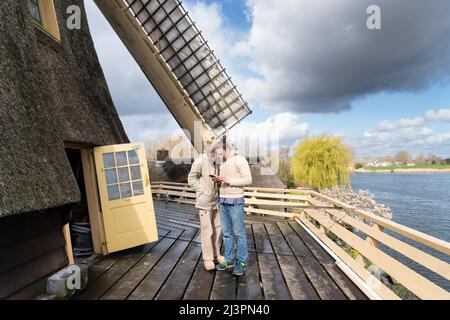 Weesp, Netherlands. 09 apr 2022. The two young volunteer millers on the platform of  windmill 'de Vriendschap' with view on river Vecht cheking their pictures and messages during a record attempt of the Voluntary Millers Guild to have all Dutch rotating wind and water turbines in the Netherlands run simultaneously between 11:00 and 12:00. More than 800 mills  participated, including 29 mills abroad. Credit: Steppeland/Alamy Live News Stock Photo