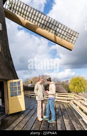 Weesp, Netherlands. 09 apr 2022. The two young volunteer millers on the platform of  windmill 'de Vriendschap' with view on river Vecht cheking their pictures and messages during a record attempt of the Voluntary Millers Guild to have all Dutch rotating wind and water turbines in the Netherlands run simultaneously between 11:00 and 12:00. More than 800 mills  participated, including 29 mills abroad. Credit: Steppeland/Alamy Live News Stock Photo