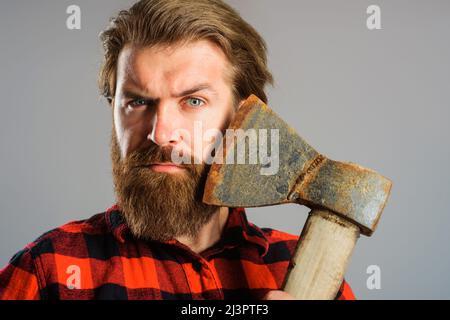 Serious bearded man with old axe. Canadian lumberjack with ax near face. Closeup portrait. Stock Photo