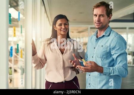Weve got big business ideas. Portrait of two happy business colleagues planning with adhesive notes against a glass wall in the office. Stock Photo