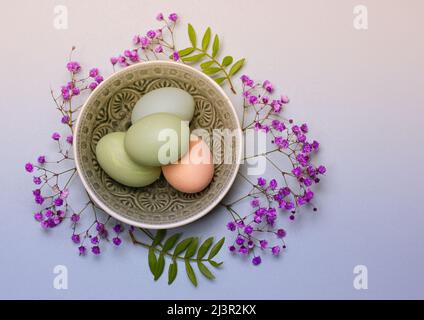 Multicolored pastel green, blue eggs lie in a round gray plate on a blue table background. Easter composition top view. Easter eggs flatly with copy s Stock Photo