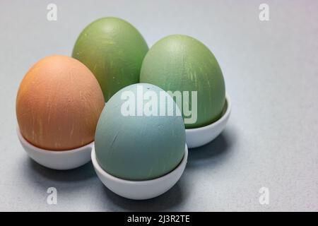 Four Easter Eggs standing in egg tray on a table on a light blue-grey background. A group of green, blue, brown colored hand-painted eggs. Traditional Stock Photo