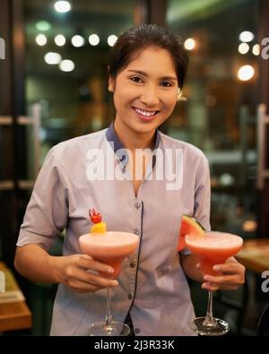 Prepare to be refreshed. Portrait of a friendly waitress carrying cocktails in a bar. Stock Photo