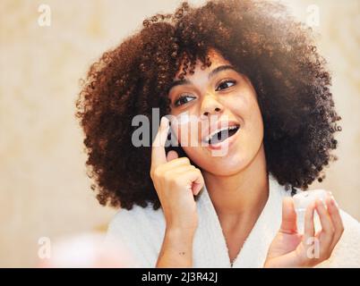 Keep your skin moisturised for the best results. Shot of a beautiful young woman applying moisturiser to her face. Stock Photo