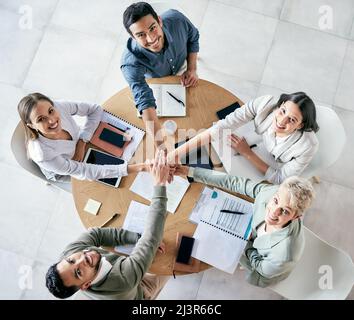 Work ethic will be reflected in everything you do. High angle shot of a group of young businesspeople joining hands in solidarity in a modern office. Stock Photo