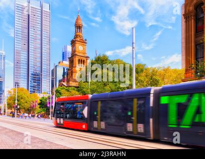 City of Sydney Town Hall house historic sandstone building with flags on the towers and public transport tram on George street. Stock Photo