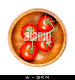 Red cherry vine tomatoes, in a wooden bowl. Ripe, small, round, cocktail tomatoes on the vine, in the size of a thumb tip, with a super sweet taste. Stock Photo